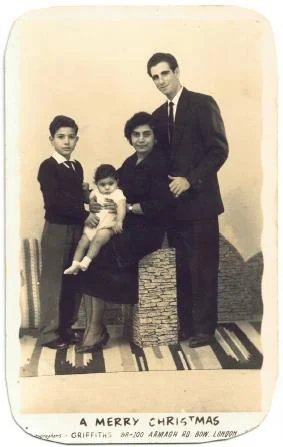 A sepia studio card printed ‘A Merry Christmas’ at the foot, showing a young man in a suit standing behind a boy, a woman and a toddler on studio steps.