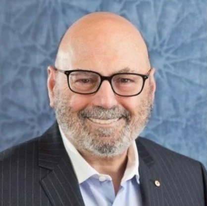 A headshot of Arthur Sinodinos, smiling, wearing glasses and a dark suit.